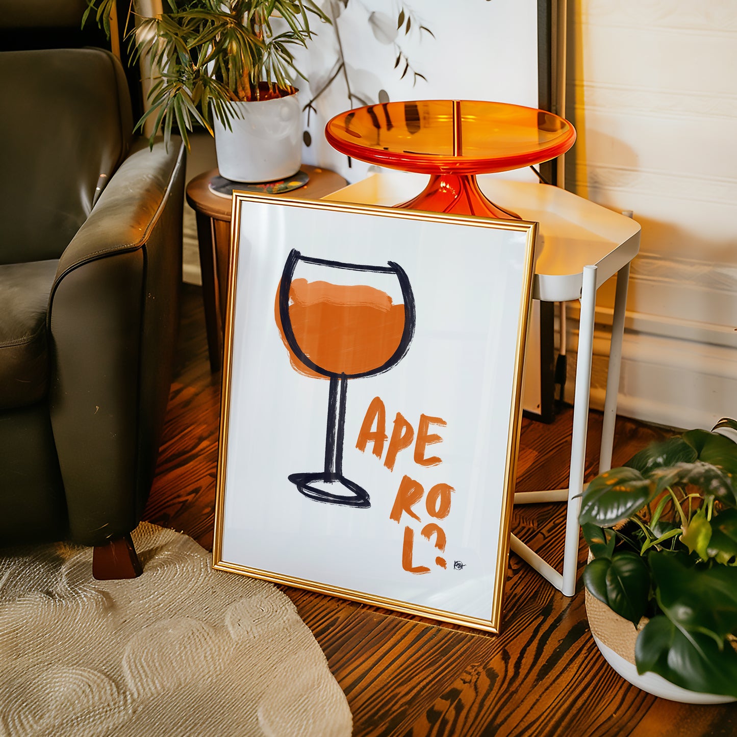 Framed artwork with a wine glass design and 'Aperol' text on a wooden floor.