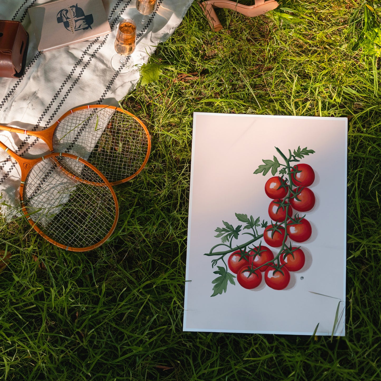 Artistic depiction of tomatoes on a white card with tennis rackets and glasses on a grassy surface.