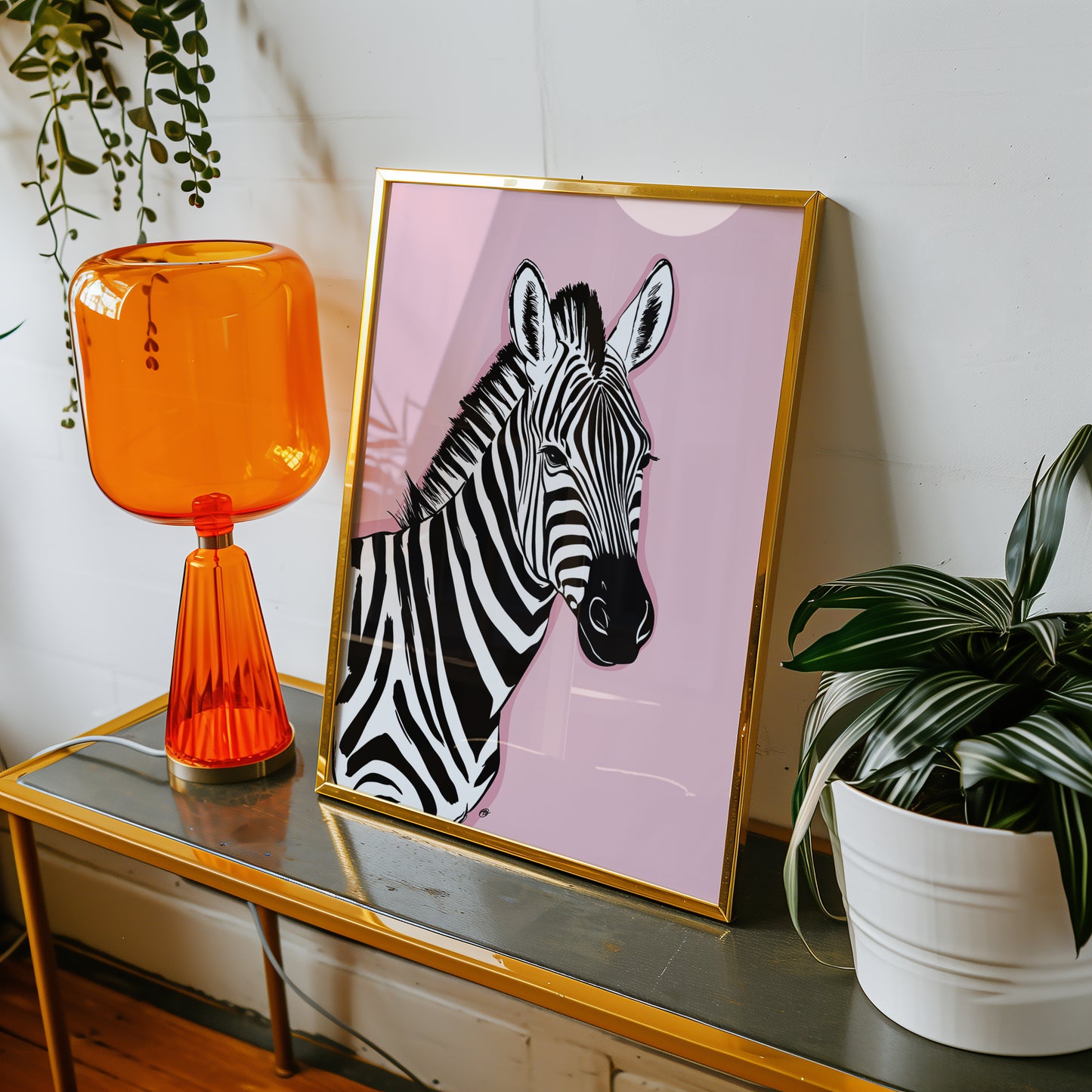Framed pink zebra print on a table with an orange lamp and plant