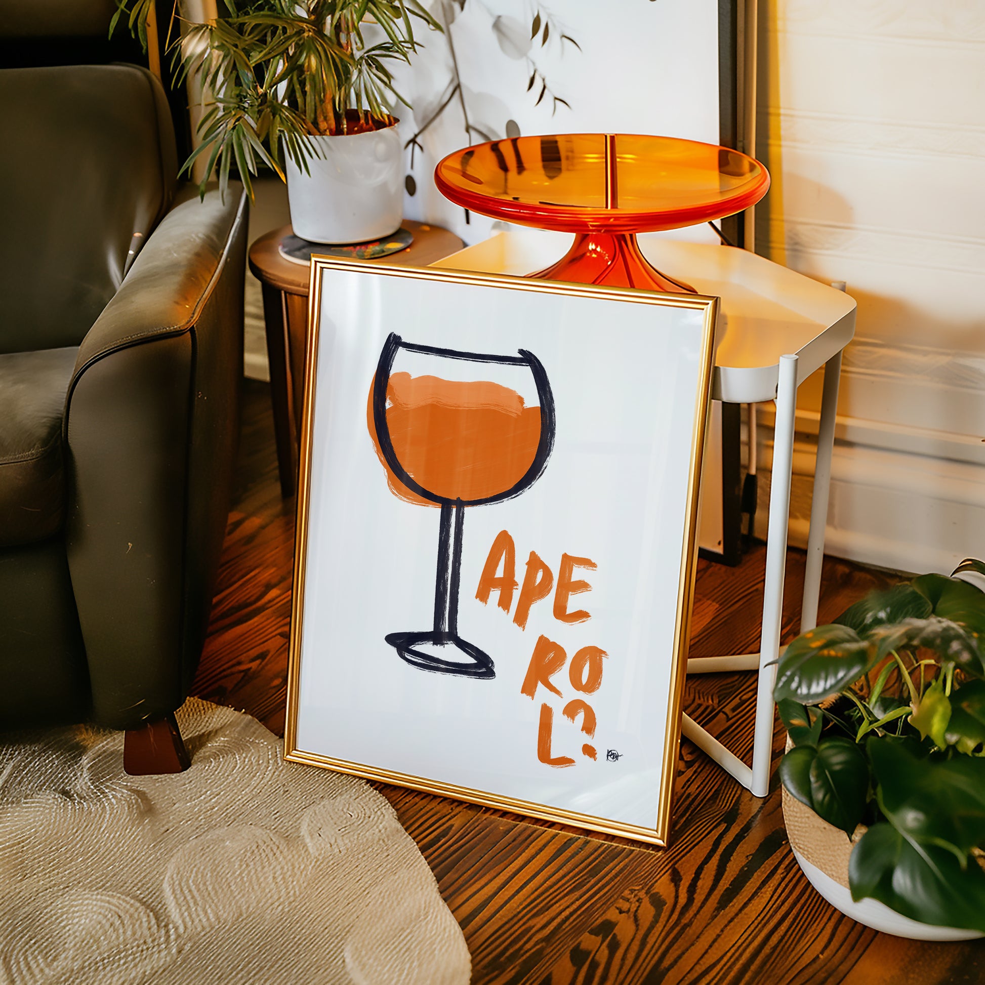 Framed artwork with a wine glass design and 'Aperol' text on a wooden floor.