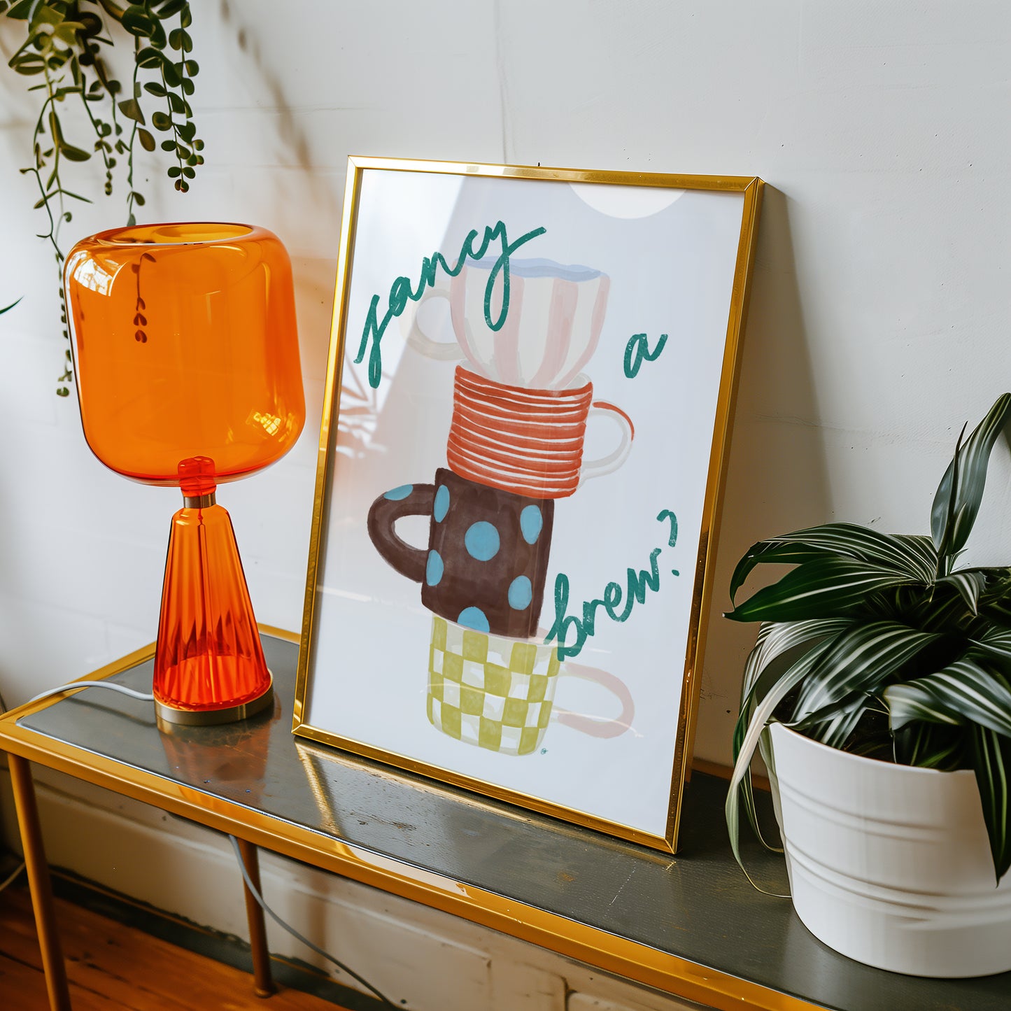 framed artwork of four colourful mugs and fancy a brew text in a retro living space with an orange glass lamp and plant