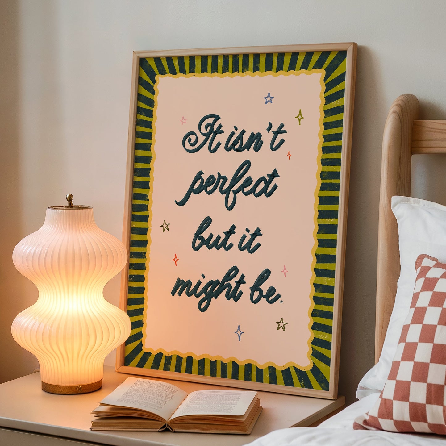 Framed quote on a nightstand next to an open book and lamp.