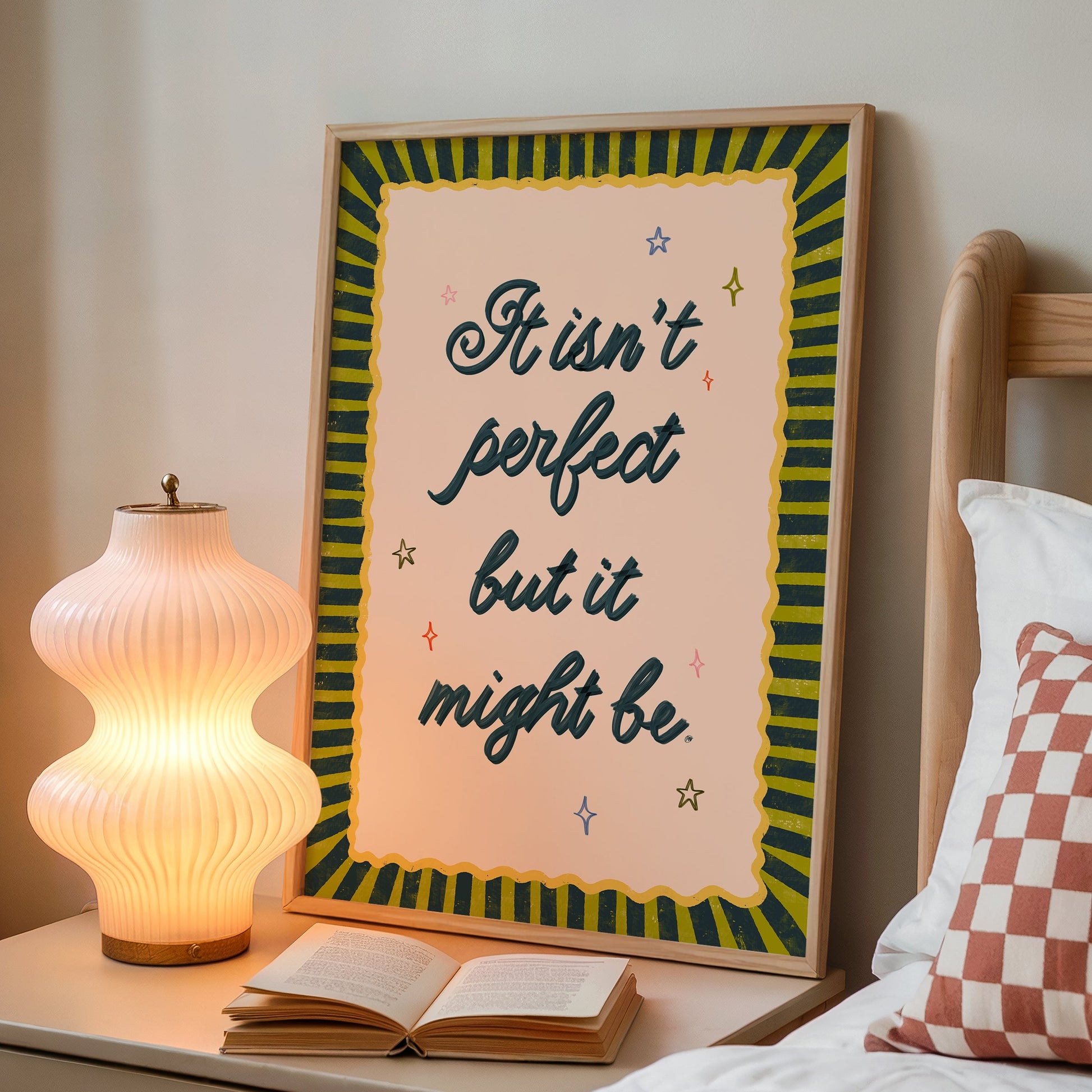 Framed quote on a nightstand next to an open book and lamp.