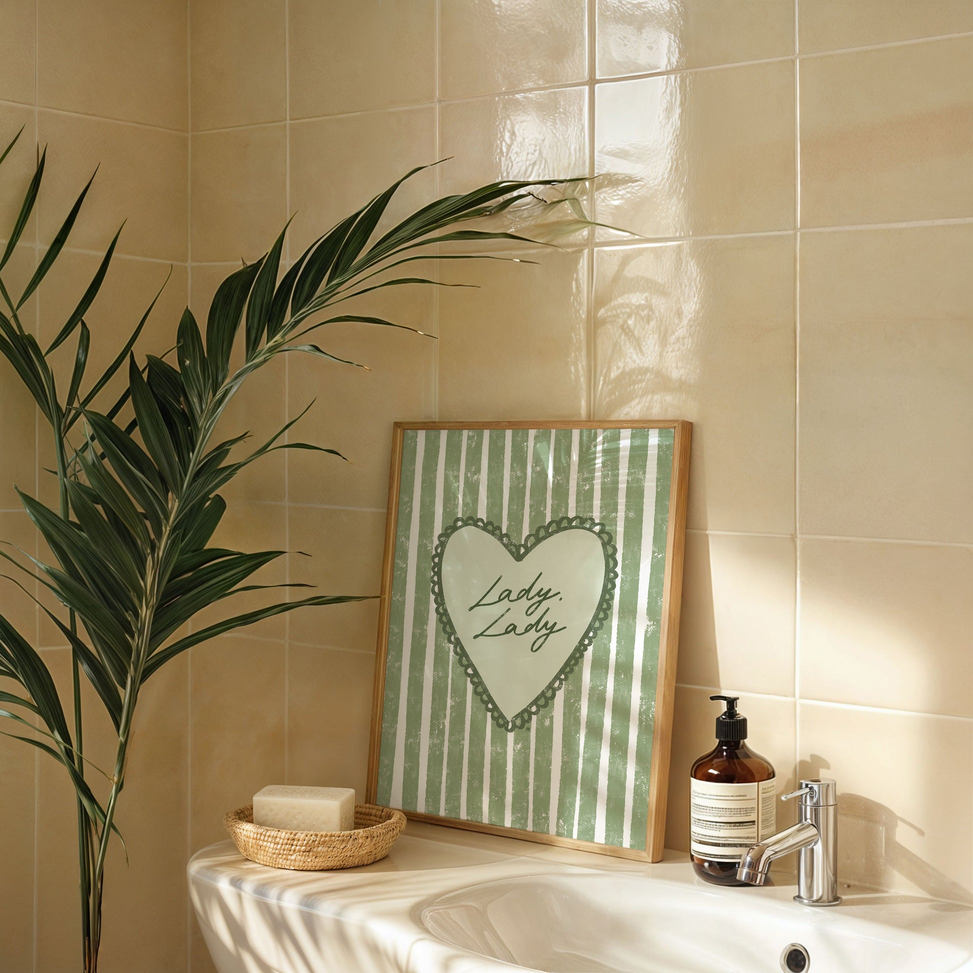 Bathroom setting with a framed picture of lady lady lyrics artwork, plant, and soap dispenser on a tiled wall.