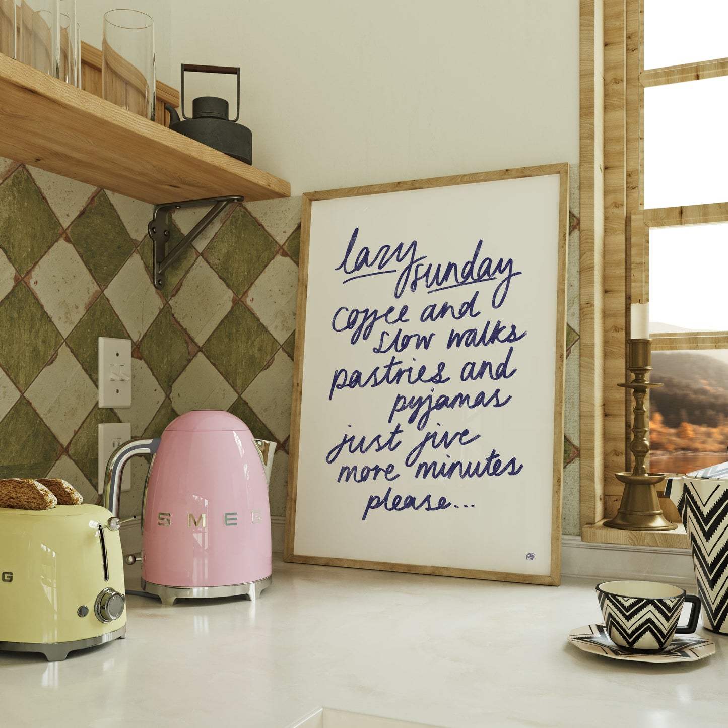 Kitchen counter with a pink kettle, yellow toaster, and framed quote about lazy sundays on a tiled wall.