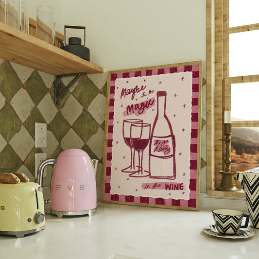framed artwork of a bottle of wine and two wine glasses with a pink checked border on top of a kitchen counter with green tiles a kettle and a toaster