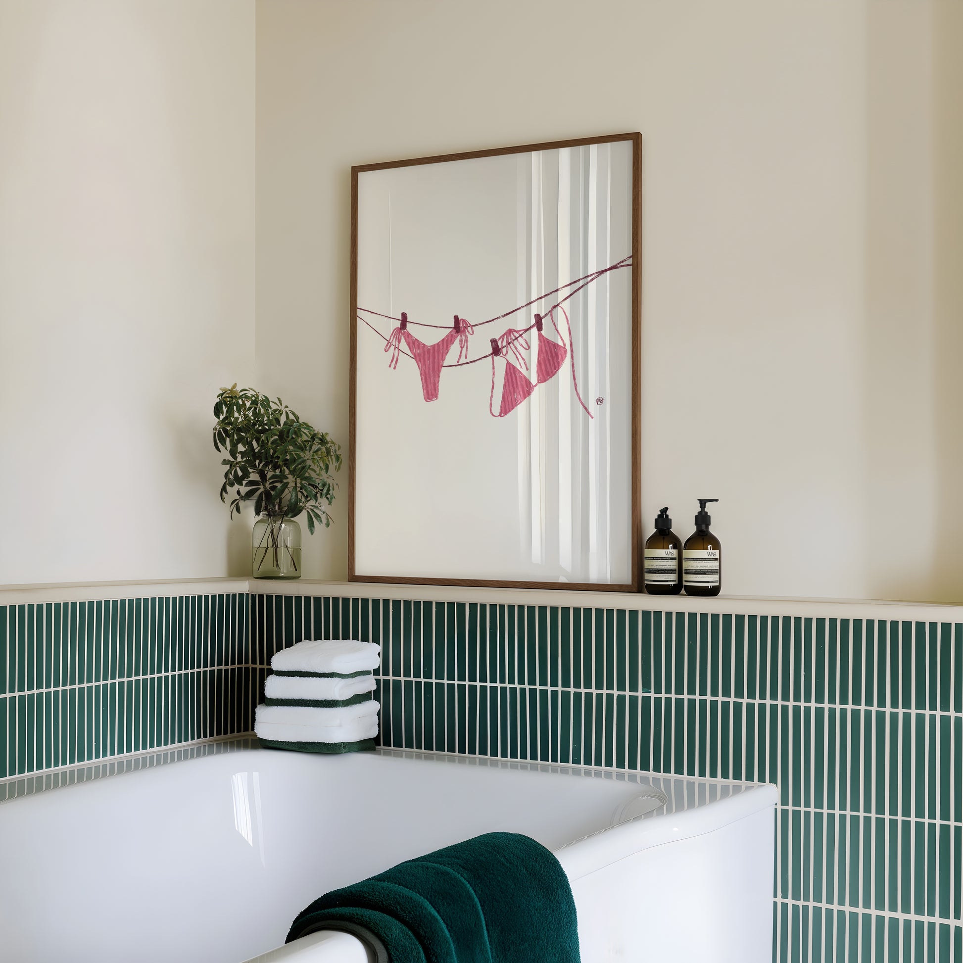 Bathroom with a framed artwork of a pink bikini on the wall, green tiles, and towels.