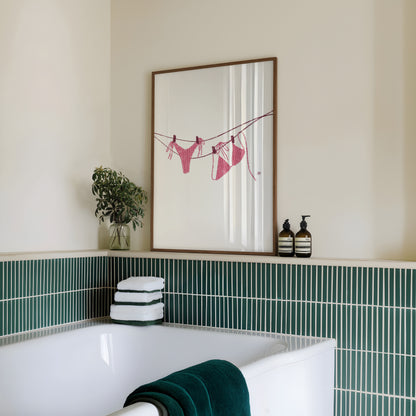 Bathroom with a framed artwork of a pink bikini on the wall, green tiles, and towels.