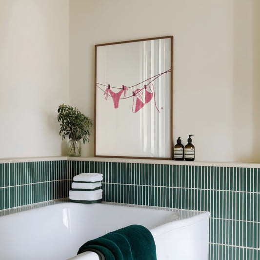 Bathroom with a framed artwork of a pink bikini on the wall, green tiles, and towels.
