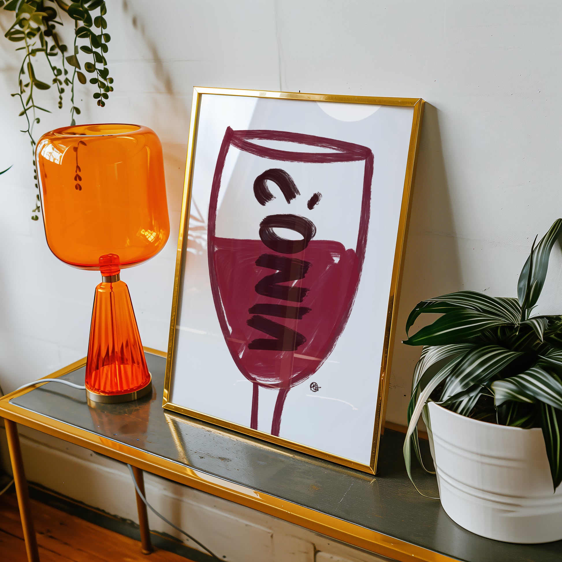 Orange glass lamp and framed artwork of a wine glass with 'VINO?' on a table with plants.