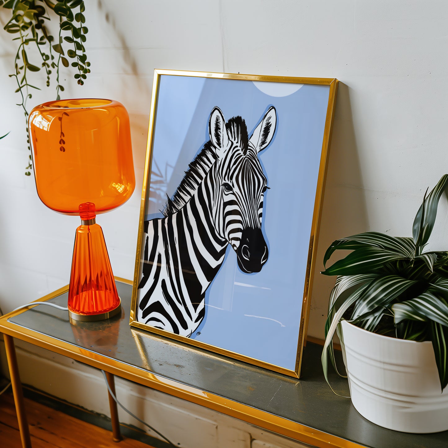 Framed blue zebra print on a table with an orange lamp and plant