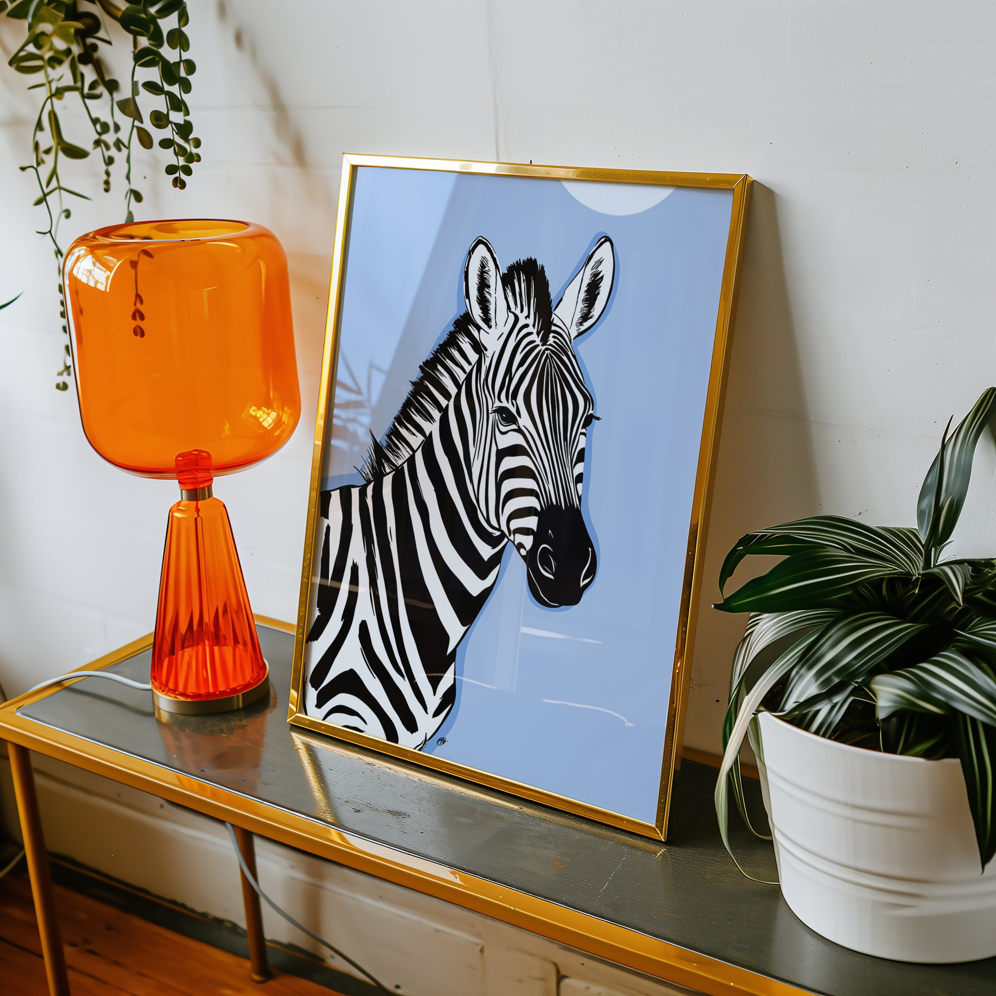Framed blue zebra print on a table with an orange lamp and plant