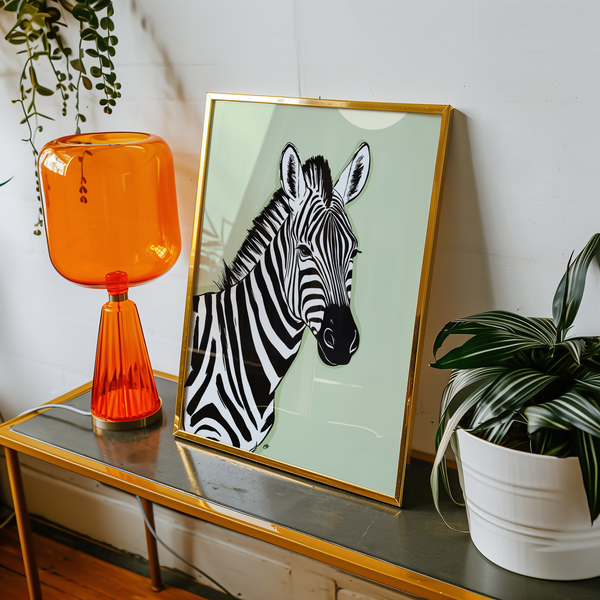 Framed green zebra print on a table with an orange lamp and plant