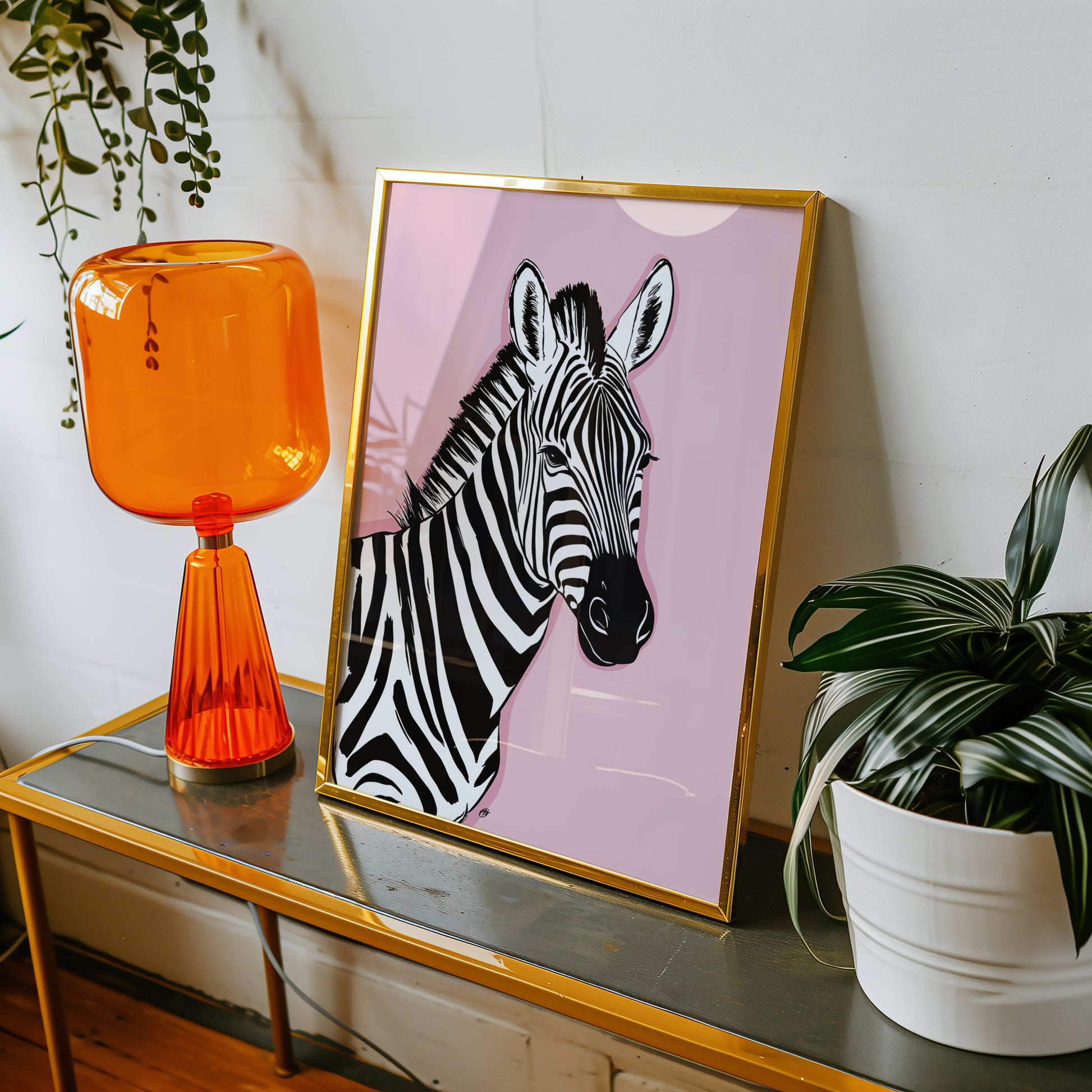 Framed pink zebra print on a table with an orange lamp and plant